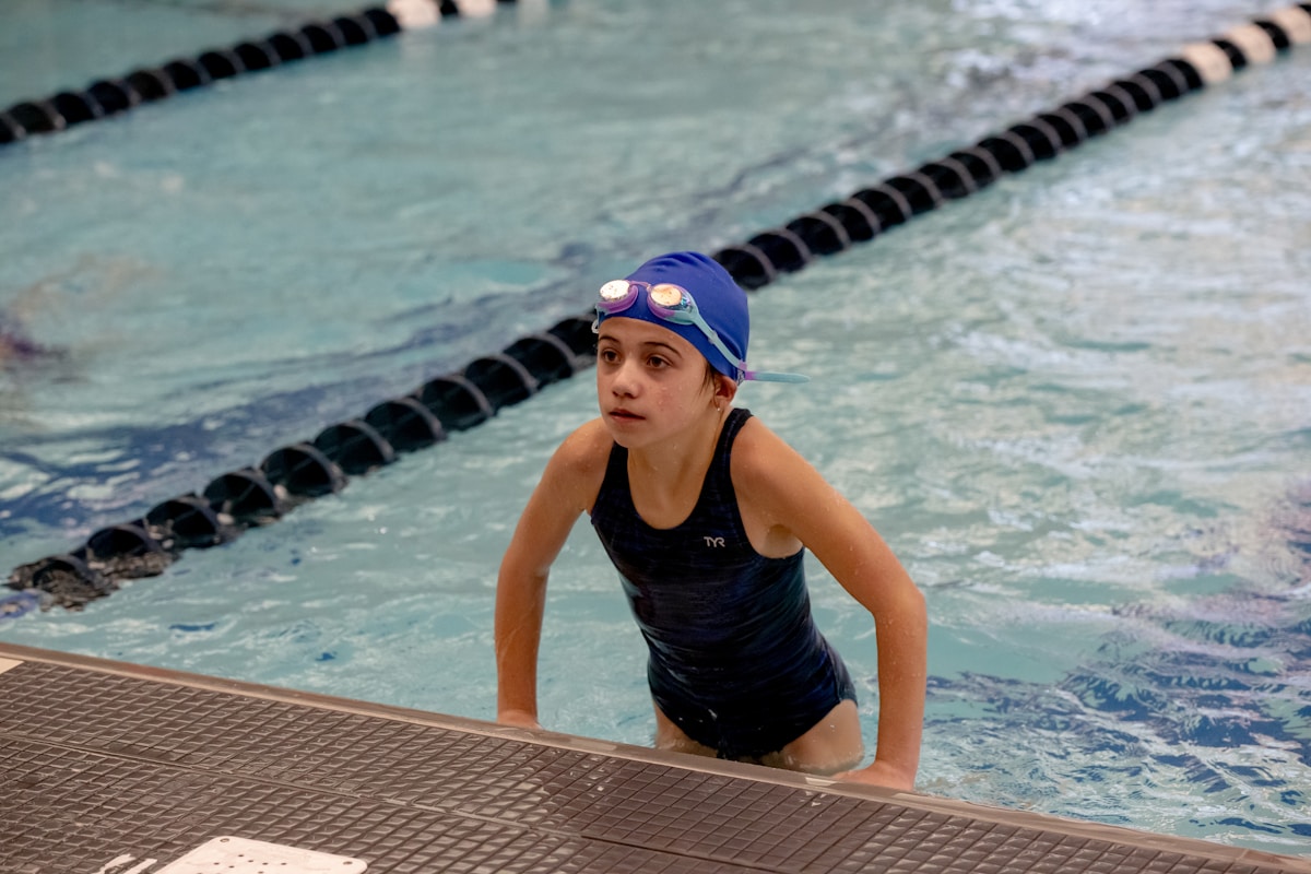 Young swimmer in blue cap climbing out of the pool after practice.