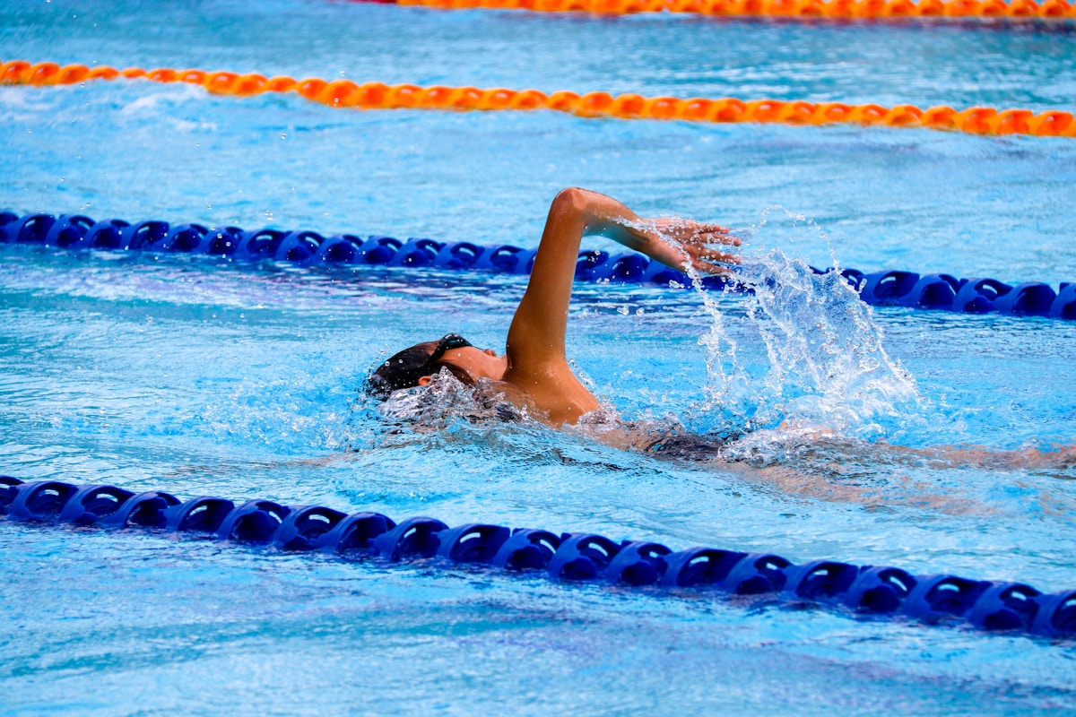 Swimmer doing backstroke in a bright outdoor pool.